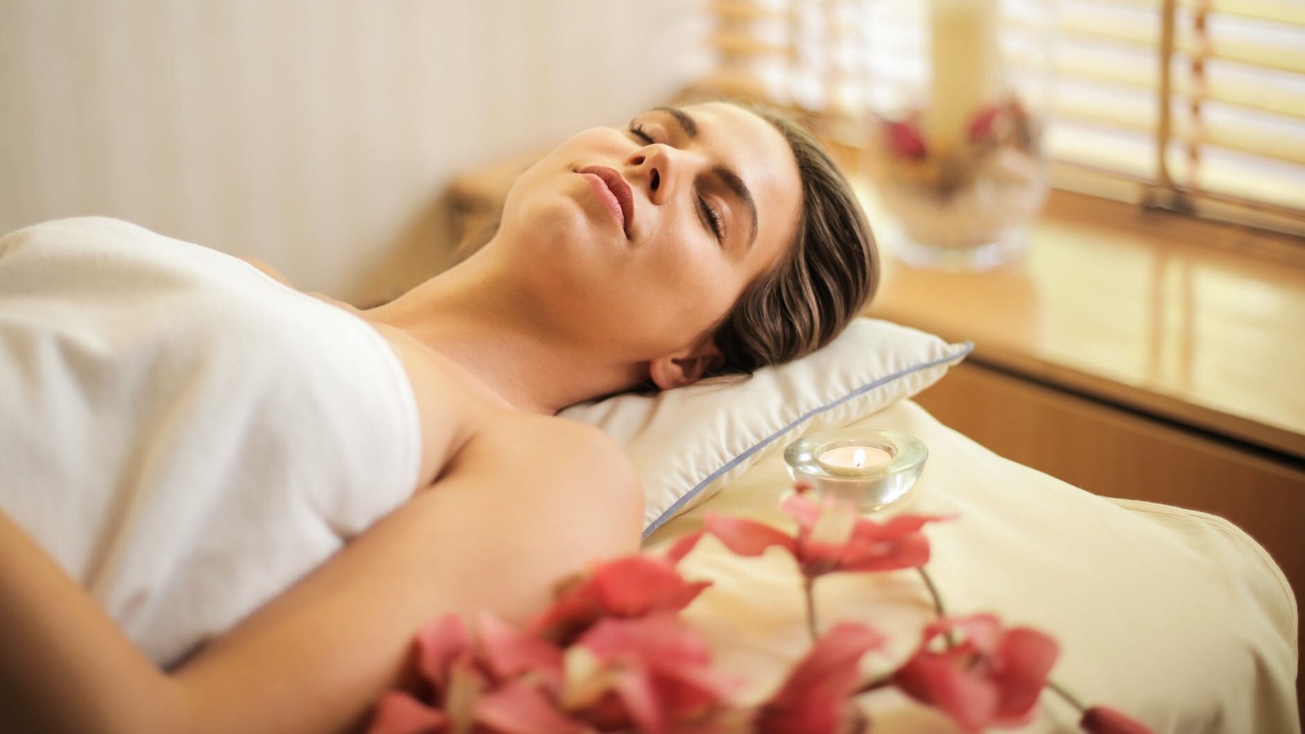 woman in wrapped in white towel lying on bed with eyes closed