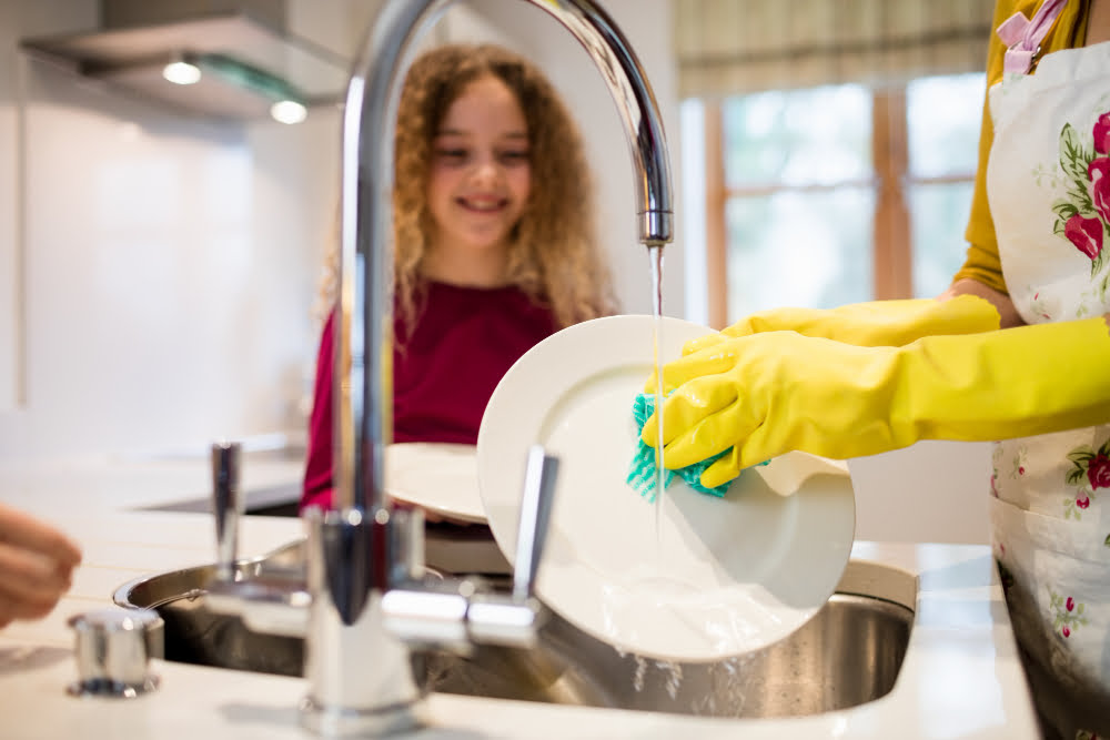 A woman holding a pair of gloves and standing in front of a clean sink.